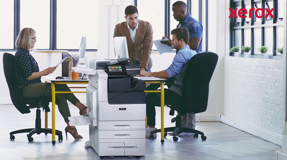 Büroangestellte arbeiten neben einem Xerox-Drucker zusammen. Büroangestellte arbeiten neben einem Xerox-Drucker zusammen.